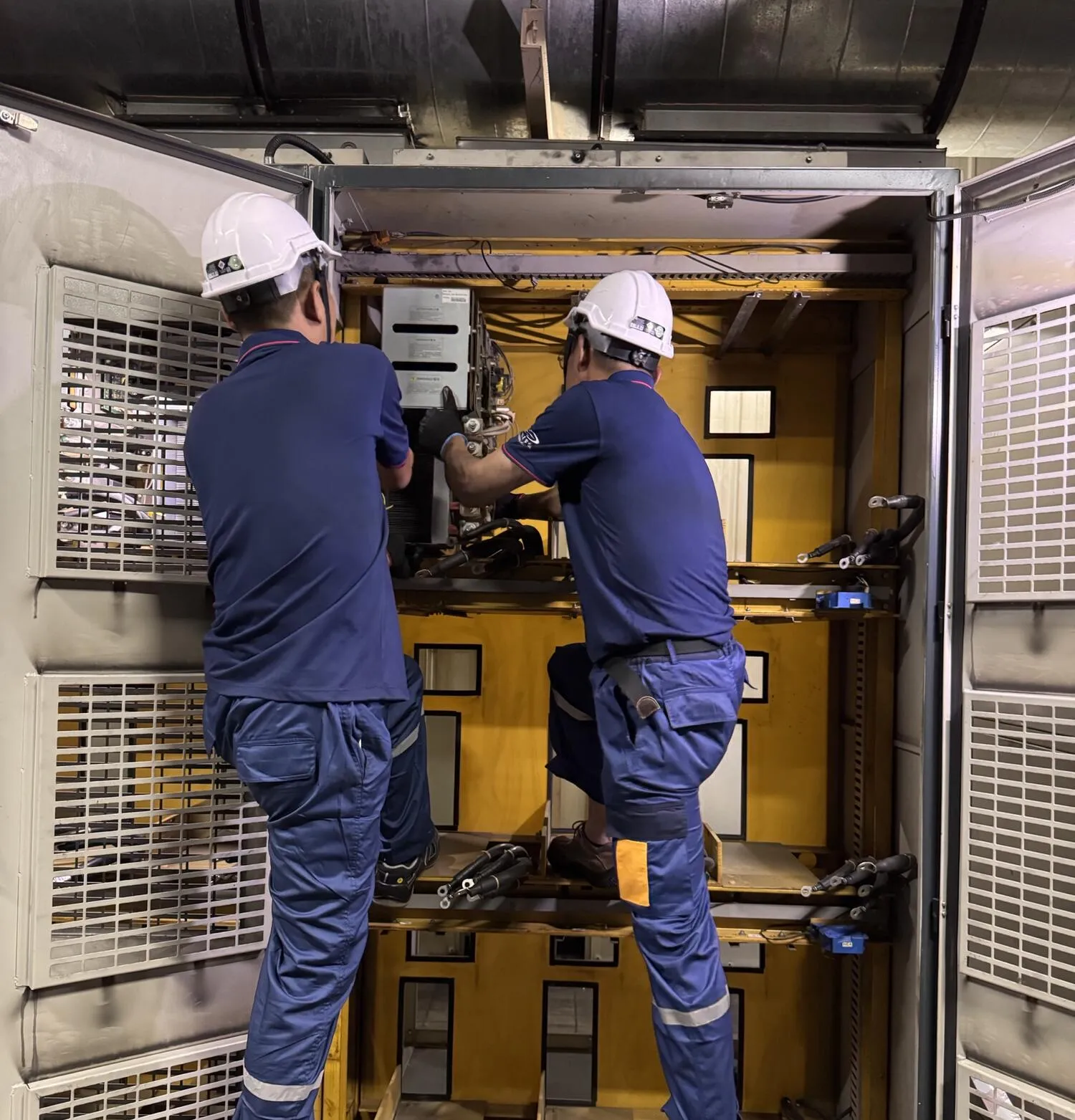 Two DUCHENG engineers in hard hats servicing a large open drive cabinet on site